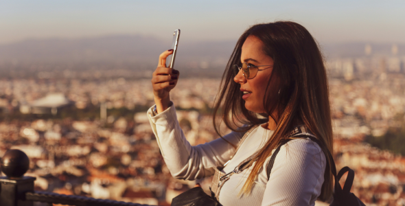 A woman stands in front of a sprawling city landscape while looking at her phone.