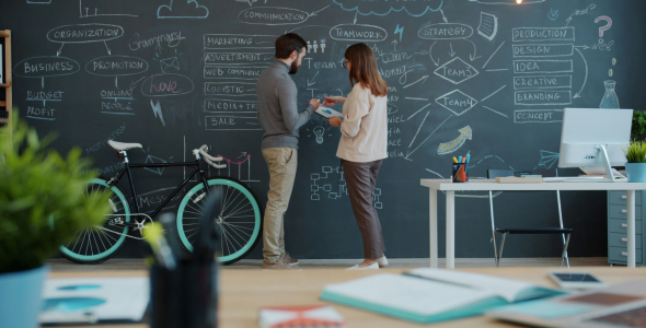 A woman and man stand in front of a blackboard filled with scriblles