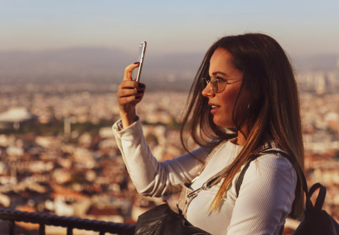 A woman stands in front of a sprawling city landscape while looking at her phone.