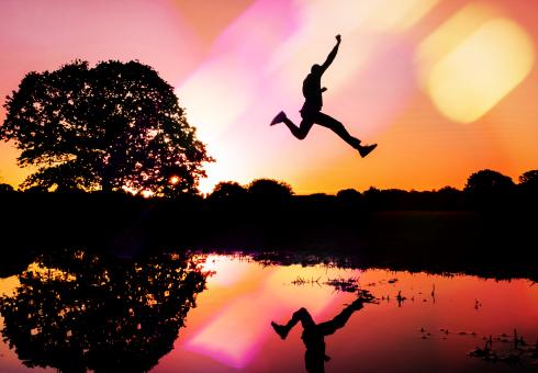 A silhouette of a man jumping over a body of water