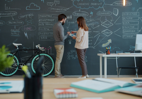 A woman and man stand in front of a blackboard filled with scriblles