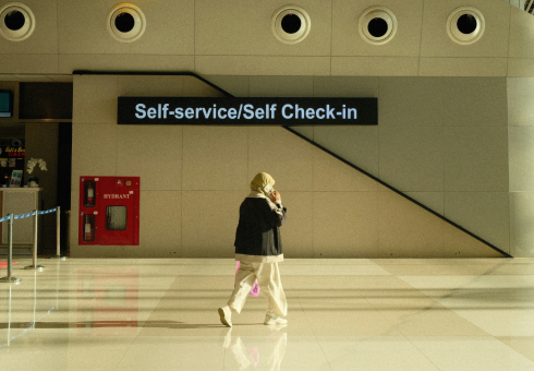 A person walks through an empty airport in front of a sign stating 'self service/self check-in'