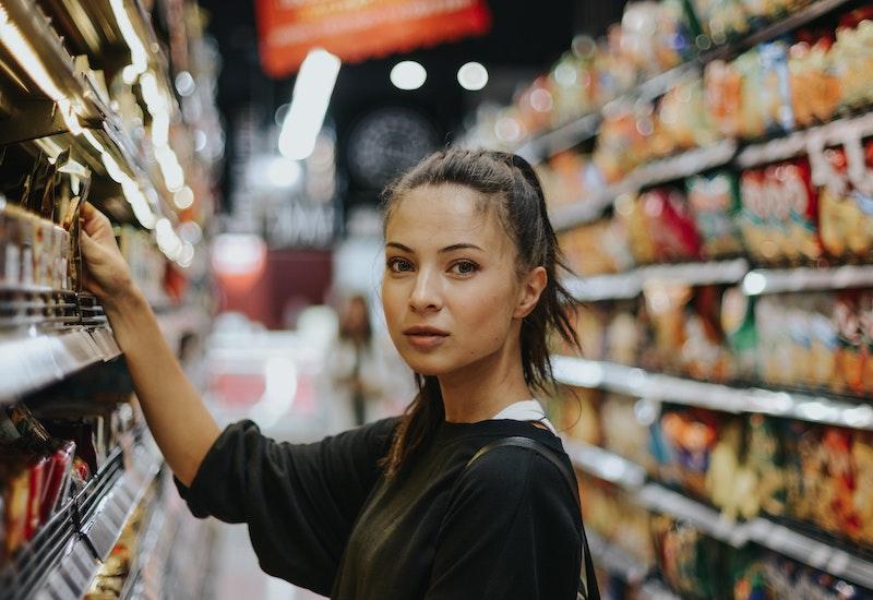 Woman shopping in a supermarket aisle, reaching for the shelves