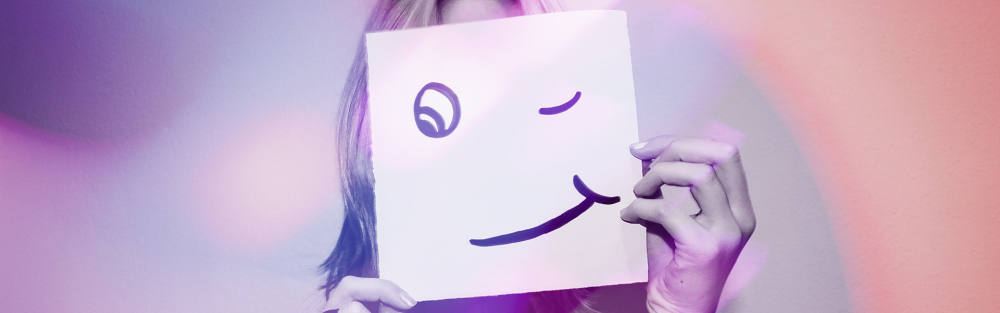 A woman hides behind a drawing of a face