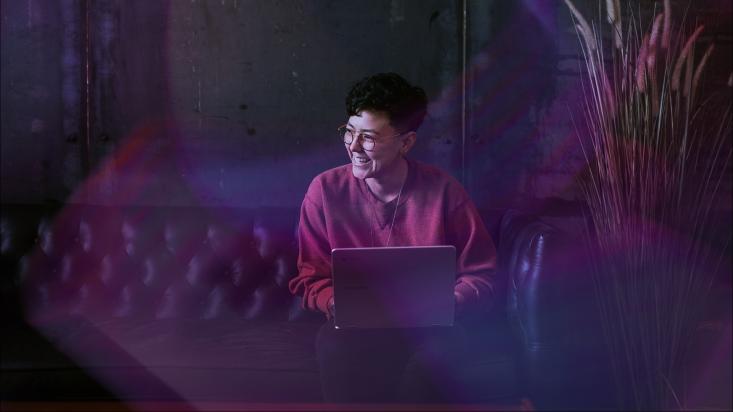 A woman sits smiling behind her laptop